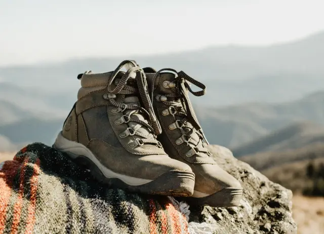 Worn brown hiking boots resting on a striped blanket draped over a rock, with hazy mountains behind